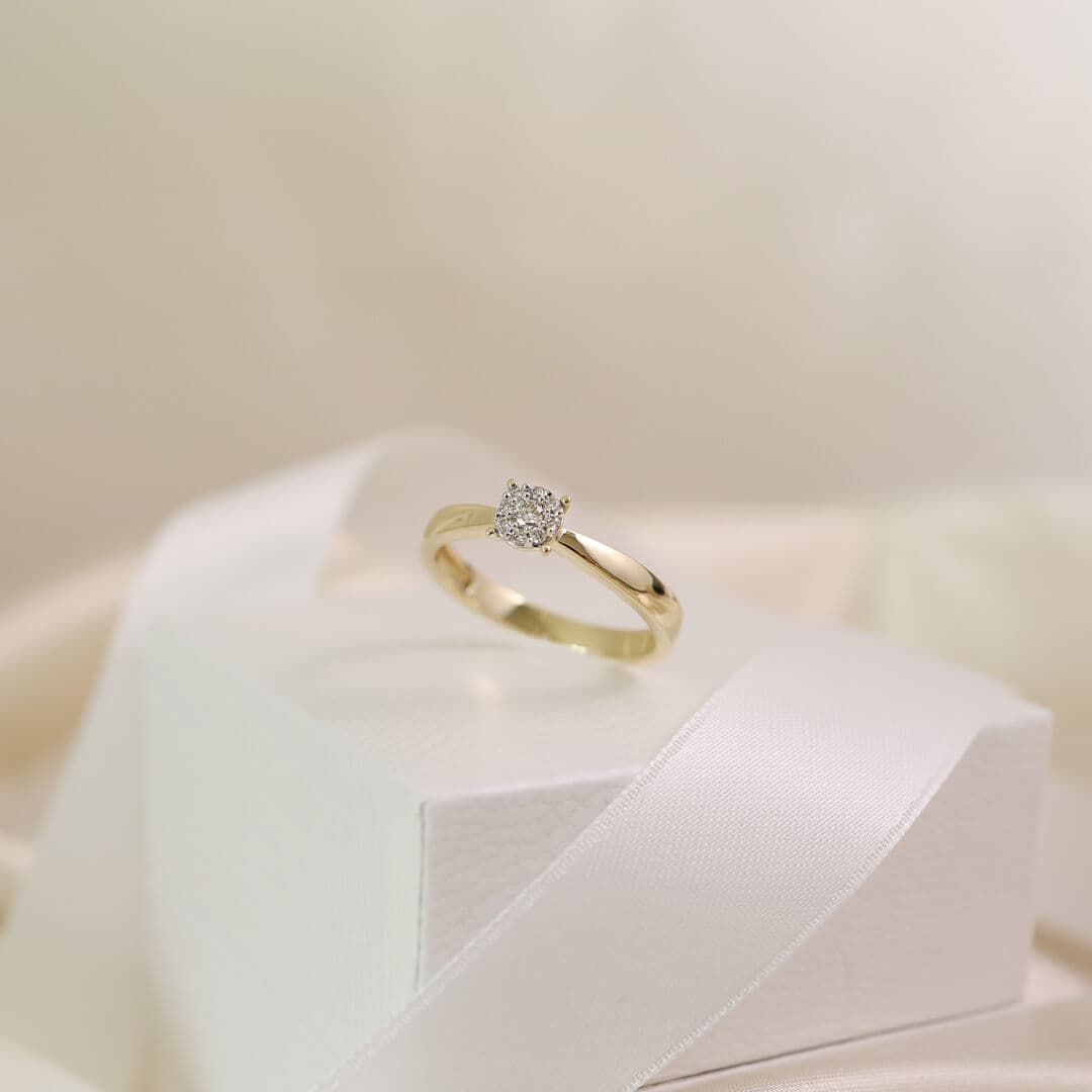 En gullring med en solitærdiamant er elegant plassert på en hvit, teksturert eske, prydet med et silkebånd.